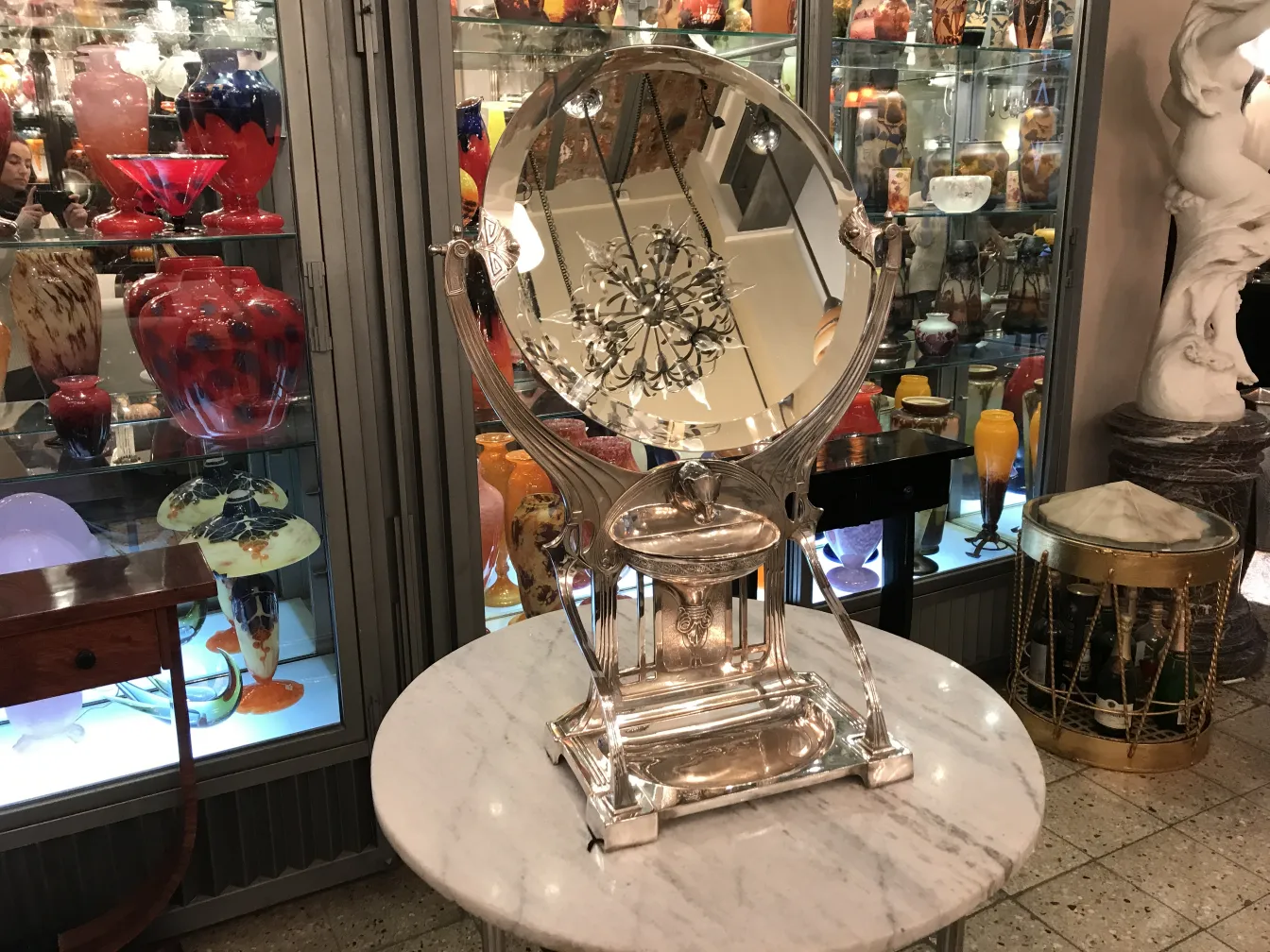 Espejo antiguo decorativo con base en estilo Art Nouveau, rodeado de objetos de colección.