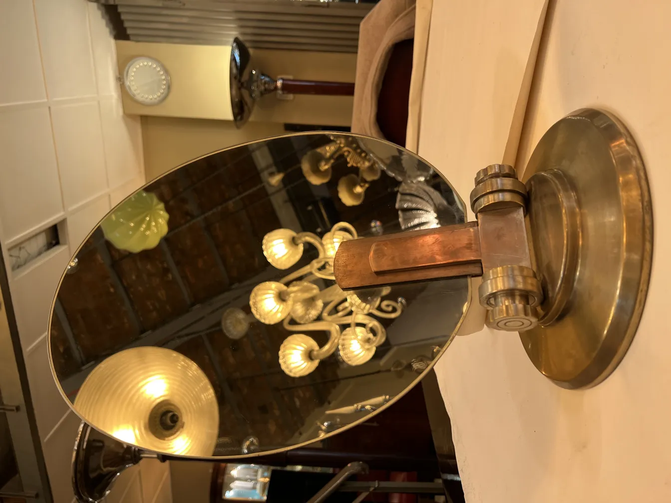Miroir ancien de style Art Nouveau avec base cylindrique, reflétant une lampe moderne.