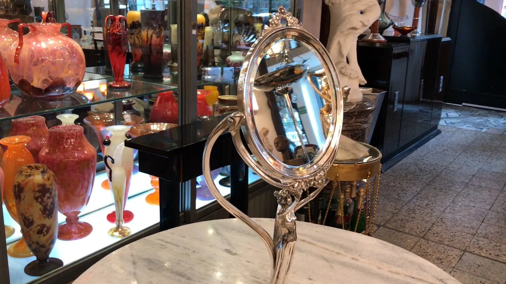 Espelho antigo com detalhes art nouveau, cercado por itens decorativos.