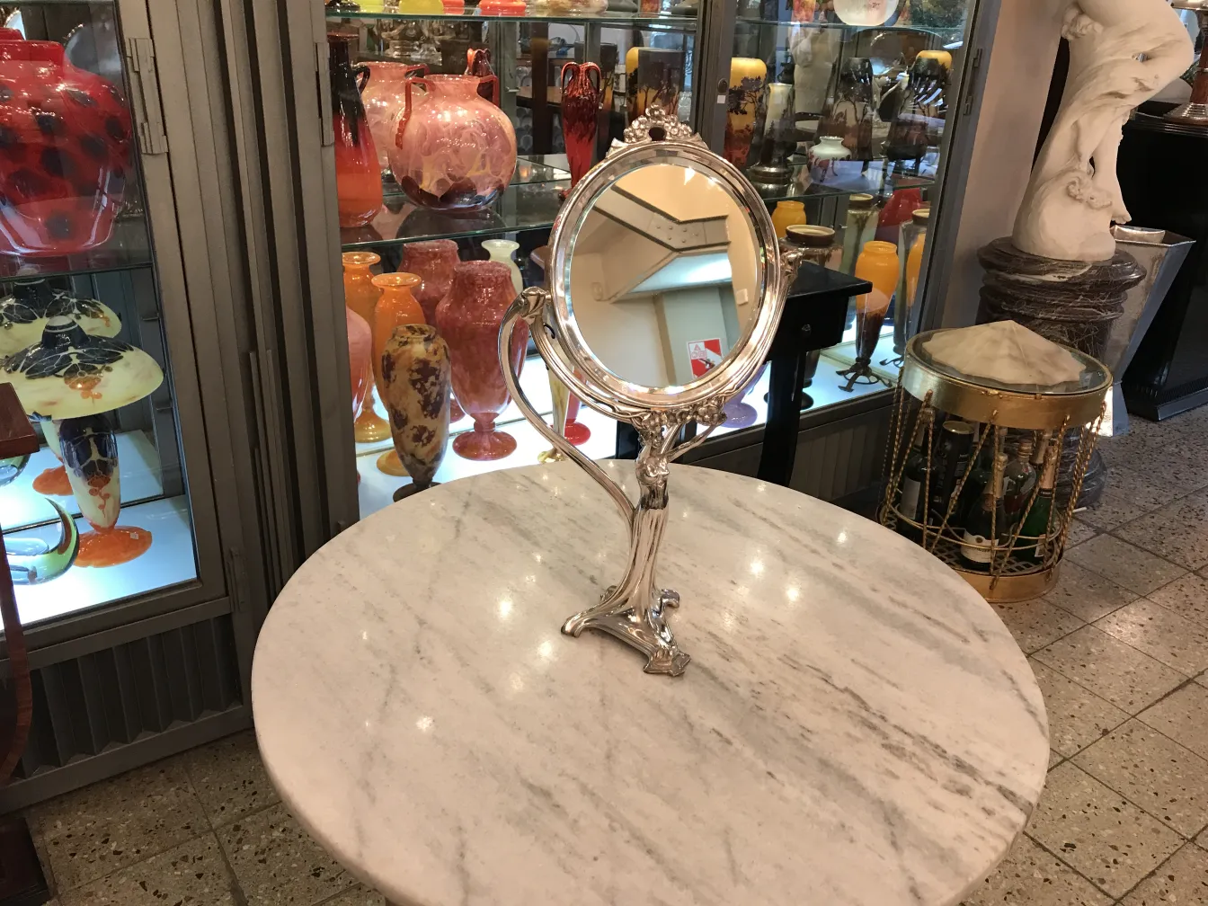 Antique mirror with art nouveau base, colorful vases in the background.