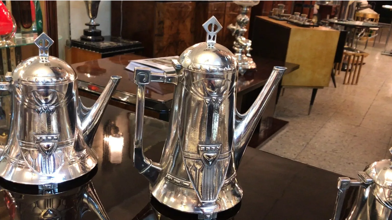 Juego de té antiguo WMF con acabado brillante, exhibido sobre mesa de madera, con otros objetos decorativos de fondo.