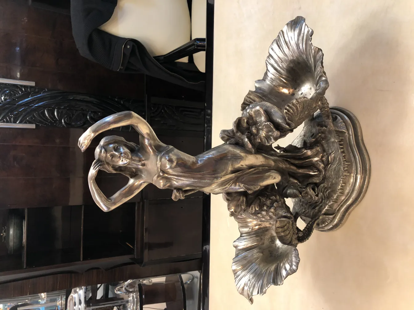 Antique centerpiece with female figure amidst decorative shells, on a dark background.