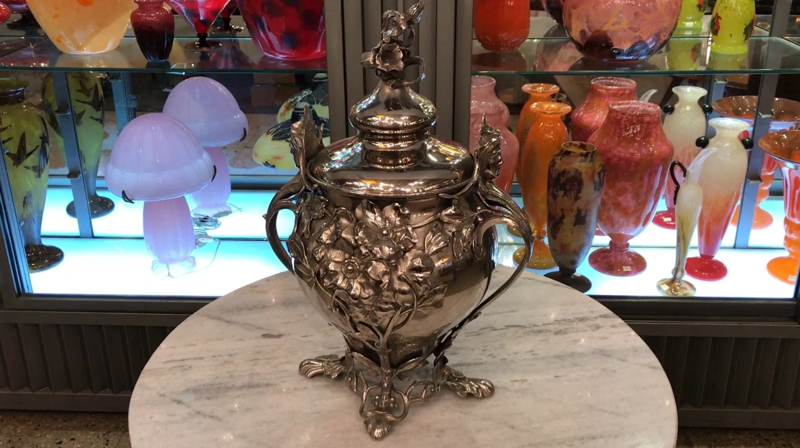 antike WMF-Bowle mit Blumendekoration und bunten Vasen im Hintergrund