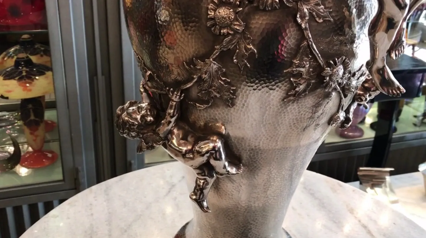 florero antiguo Orivit con un niño sosteniendo flores, decorado con hojas y flores.