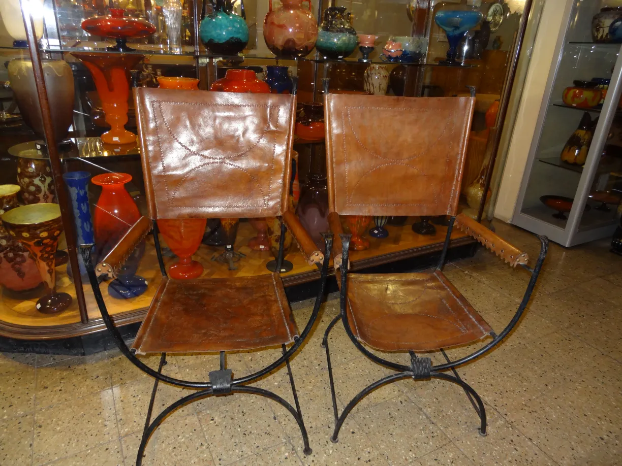 Dos sillones antiguos con un diseño clásico y detalles artesanales delante de una estantería de vidrio colorido.