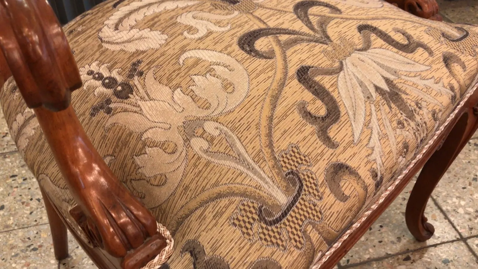 Vista detalhada de 3 poltronas antigas com estofamento floral e braços decorativos.