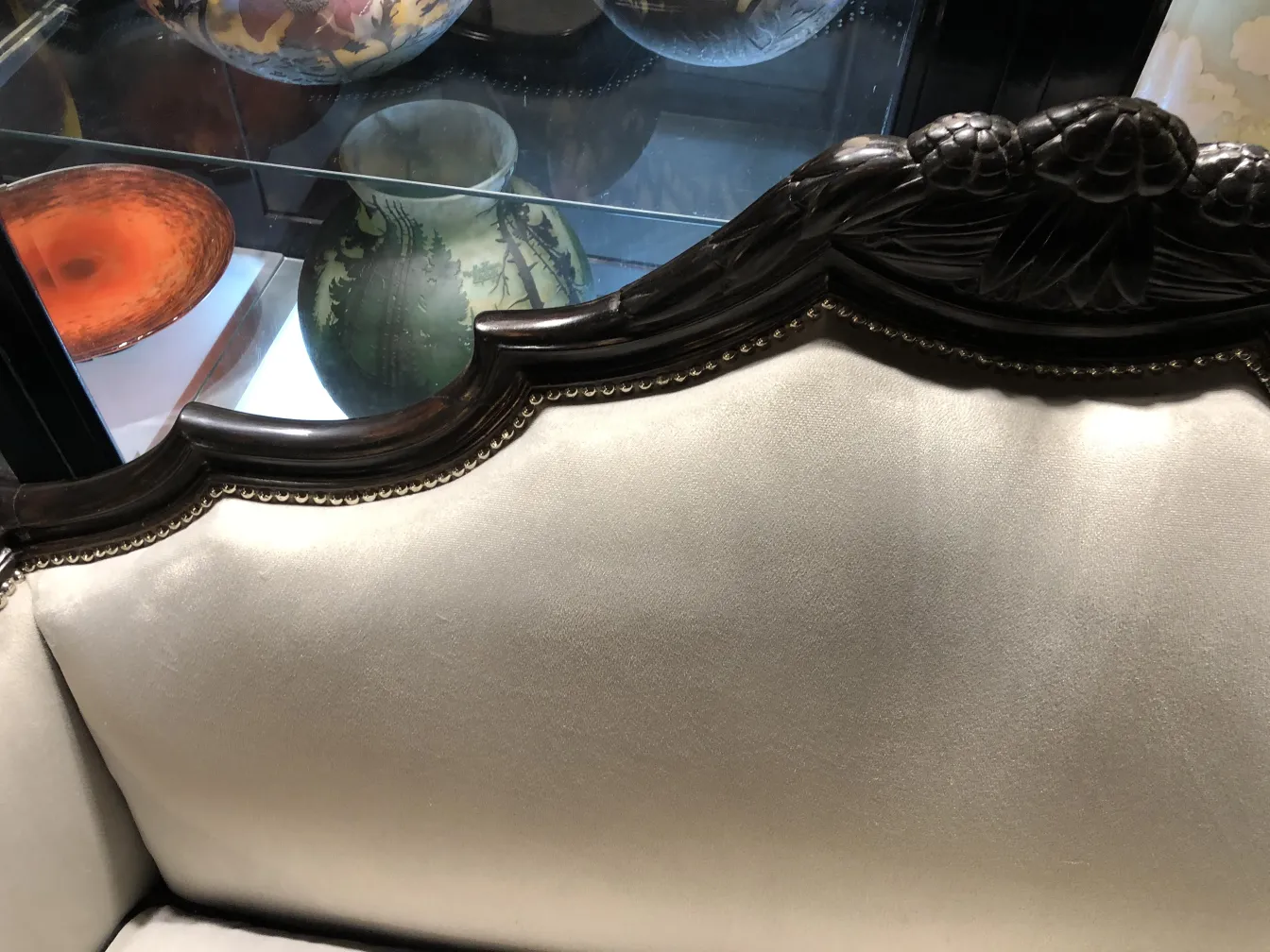 Vista parcial de uma poltrona antiga com detalhes ornamentais e fundo de antiguidades