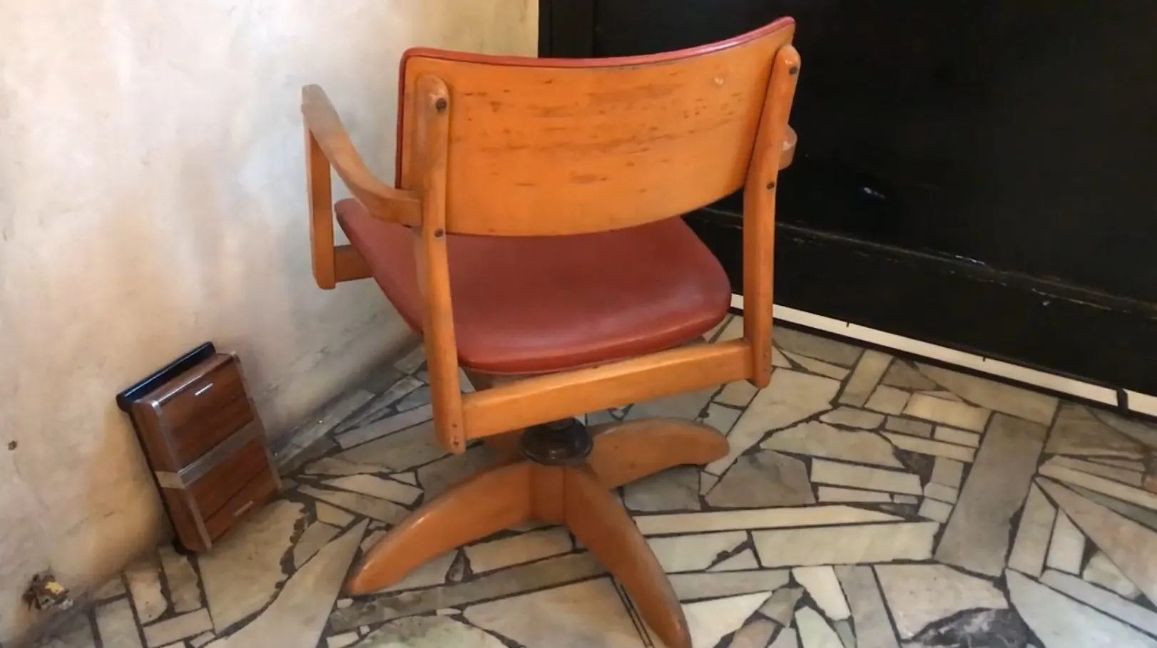 Fauteuil de bureau antique avec base en étoile et revêtement rouge dans un environnement de sol en mosaïque.