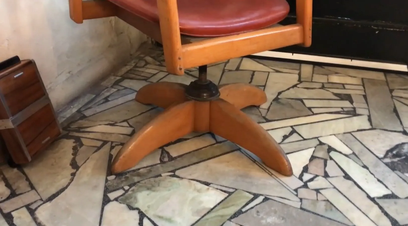 Античное офисное кресло с простым функциональным дизайном, вращающаяся основа и красная обивка, расположенное в уютной обстановке.