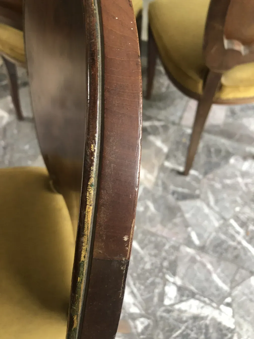 Visão lateral de uma cadeira antiga jansen com estofamento amarelo, em um ambiente com mais cadeiras.