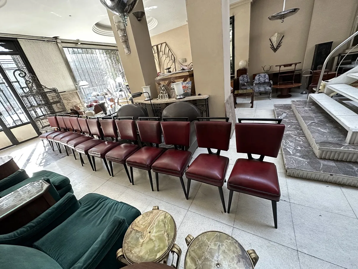 عرض لـ 12 كراسي قديمة في غرفة مشرقة محاطة بأثاث قديم آخر.