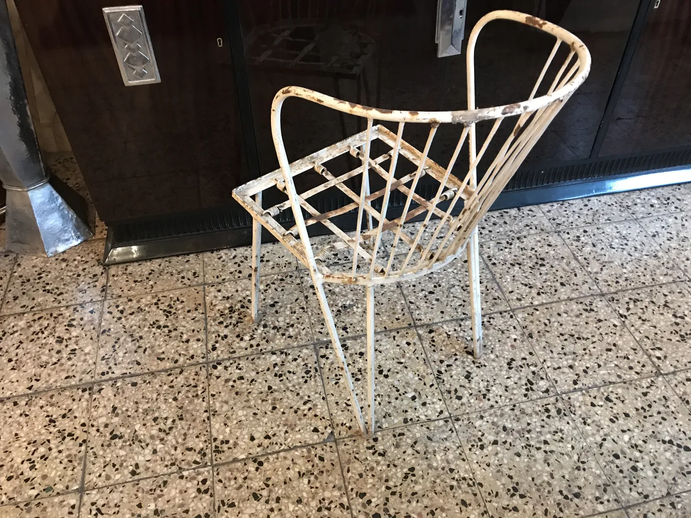 Silla de jardín antigua con un diseño de rejilla y desgaste visible, de color claro.