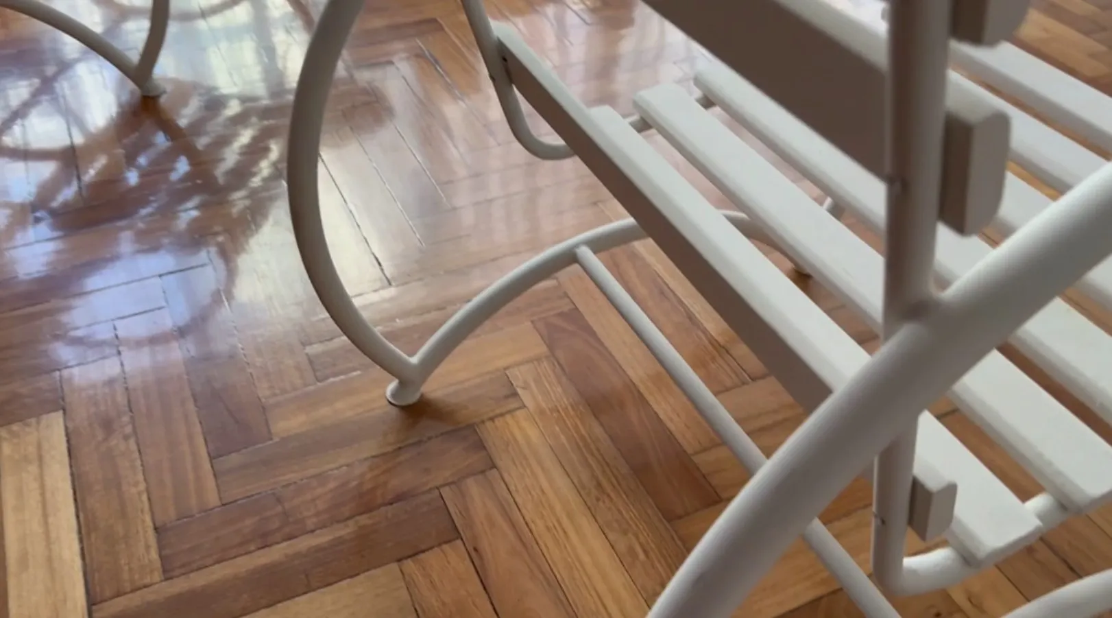 Visualização de 2 poltronas de jardim antigas com acabamento claro, sobre um piso de madeira brilhante.