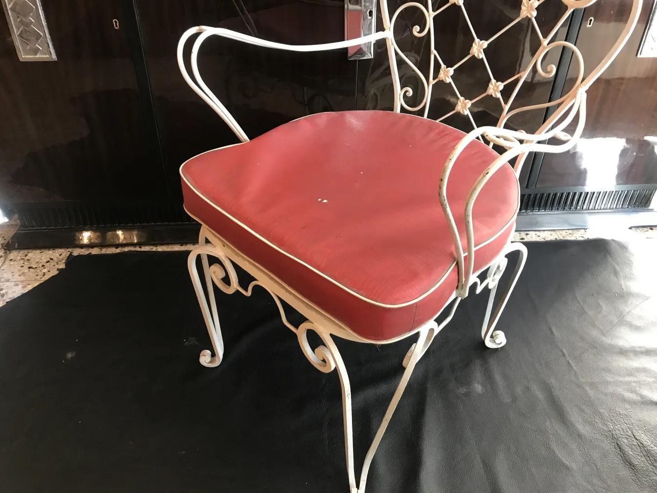 Antique garden armchairs with red cushions on a dark background.