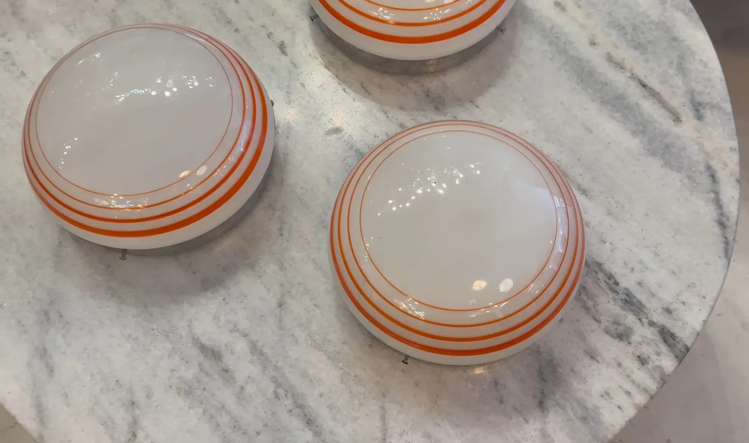 tres plafones antiguos de forma redonda con bandas naranjas, sobre un fondo de mármol claro