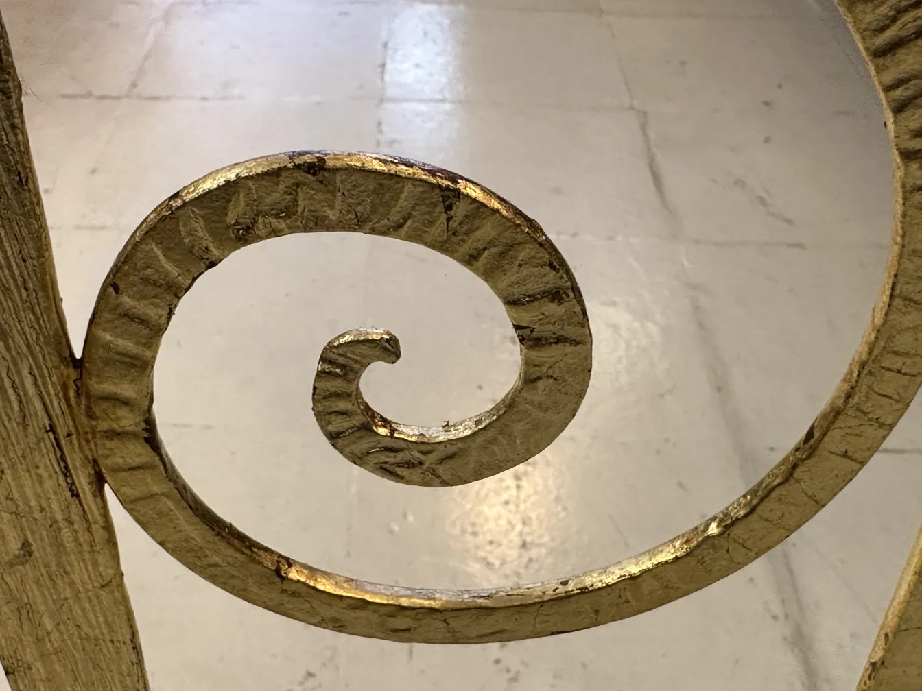 Detail eines antiken Schirmständers mit spiralförmigem Golddesign auf hellem Hintergrund.