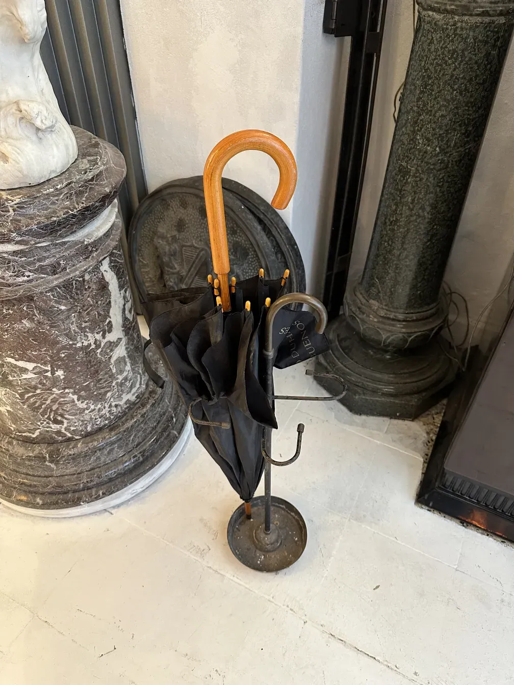 Portaombrelli antico con ombrello nero e manico di legno in ambiente decorativo