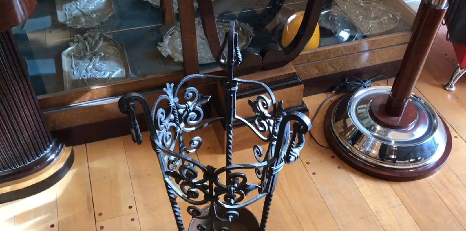 Antiguo paragüero decorativo con diseño ornamentado en hierro, pintado en negro, contexto de un ambiente elegante con antigüedades.