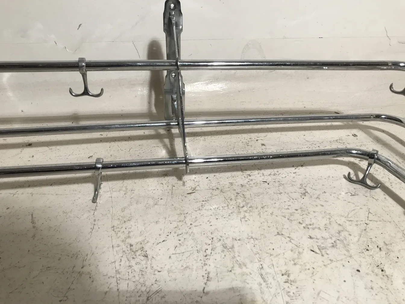 Antique coat rack with metal structure and multiple hooks in a neutral setting.