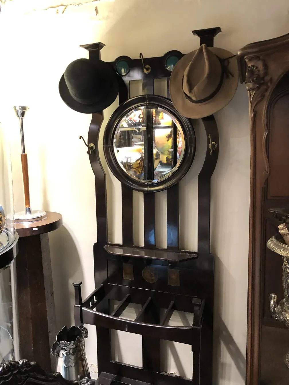 Attaccapanni antico con dettagli decorativi e specchio rotondo. Include ganci e cappelli come parte dell'ambiente.