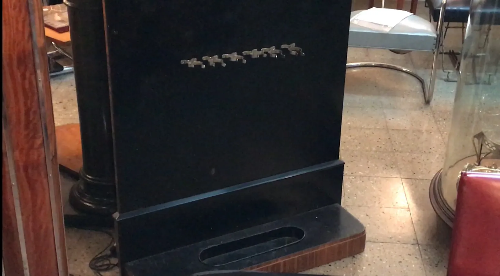 antique coat rack in dark color with hooks on front, set in antique environment