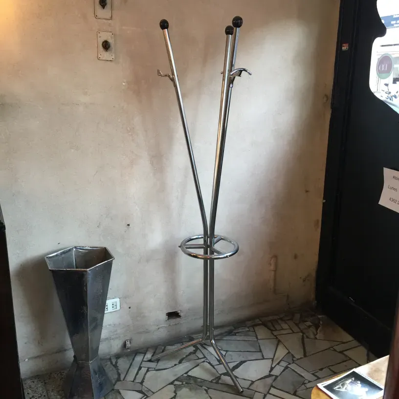 Antique standing coat rack with hooks and circular base. Wall background and stone floor.