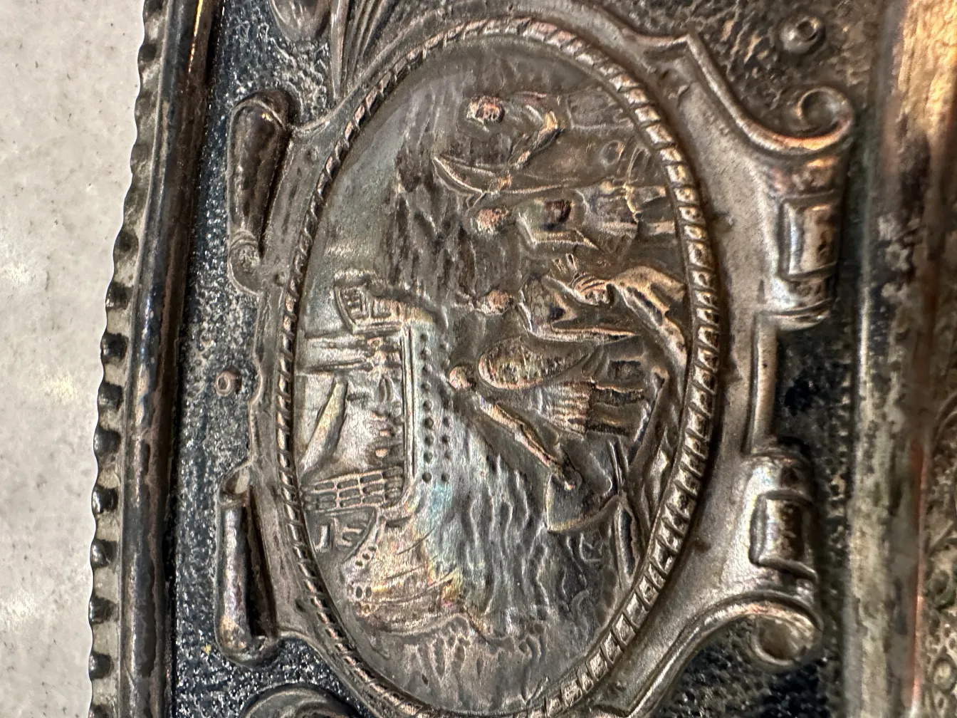 Placa de pared antigua con una escena marítima de barcos y personas.