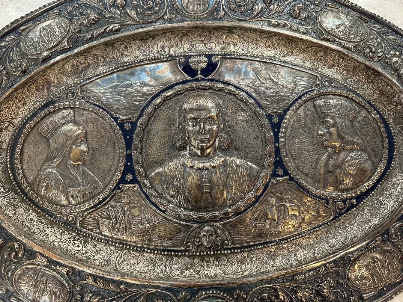 Plaque murale antique présentant des portraits décoratifs et des bateaux.