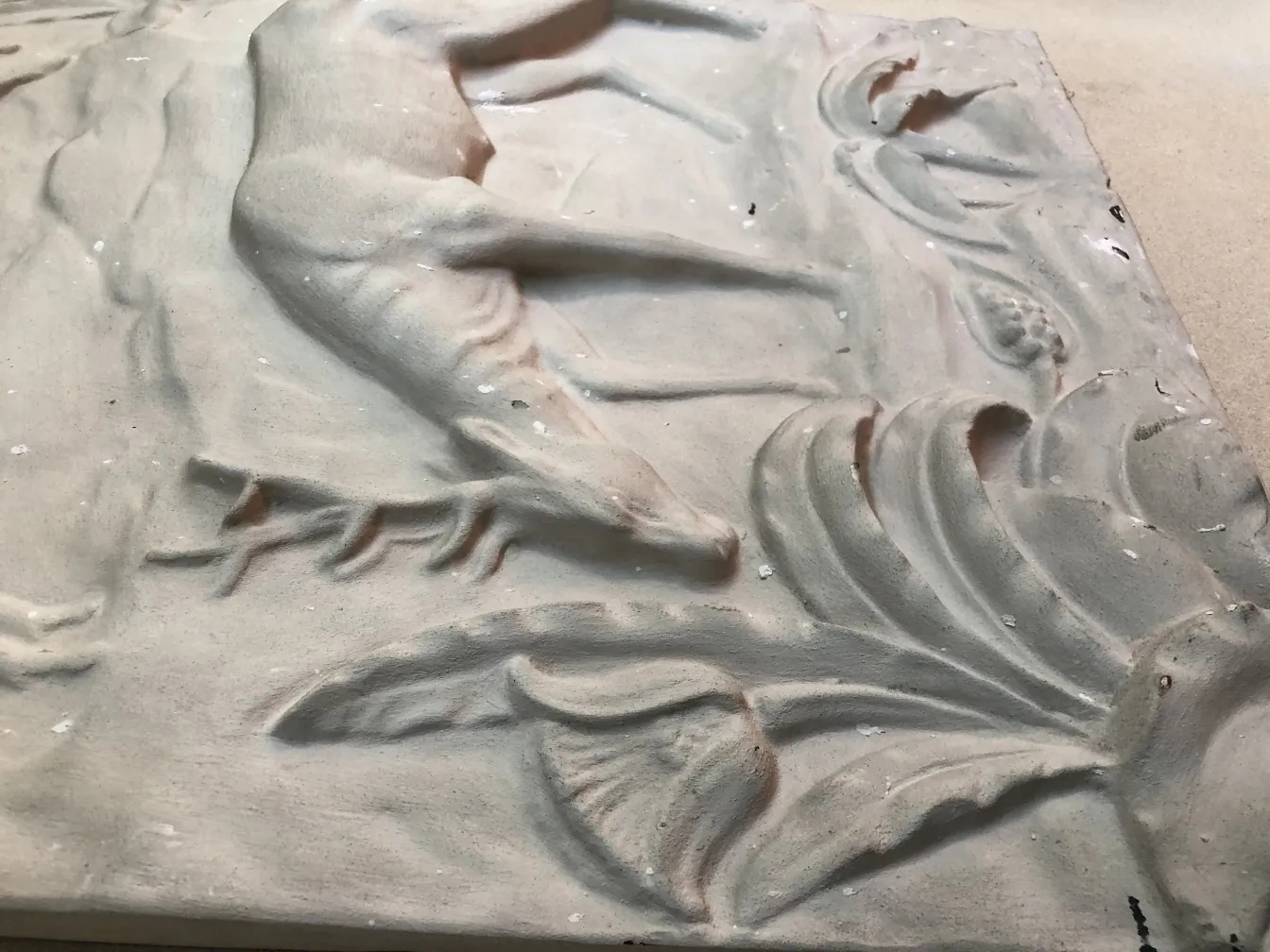 Antike Wandplatte mit floralem und blattförmigem Relief auf hellem Hintergrund.