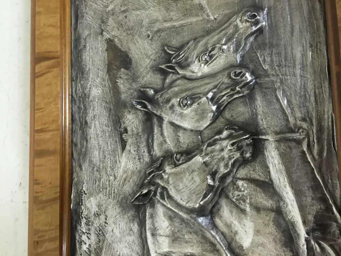 Plaque murale ancienne avec un design de chevaux en relief.