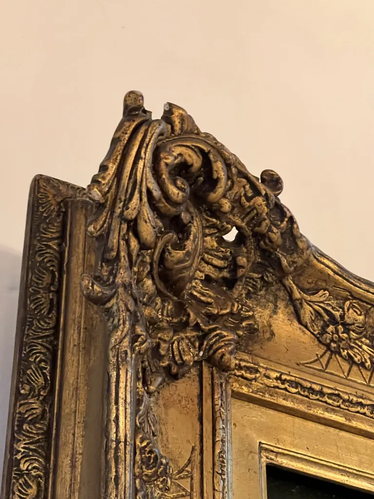 Peinture ancienne avec un cadre doré aux détails complexes.