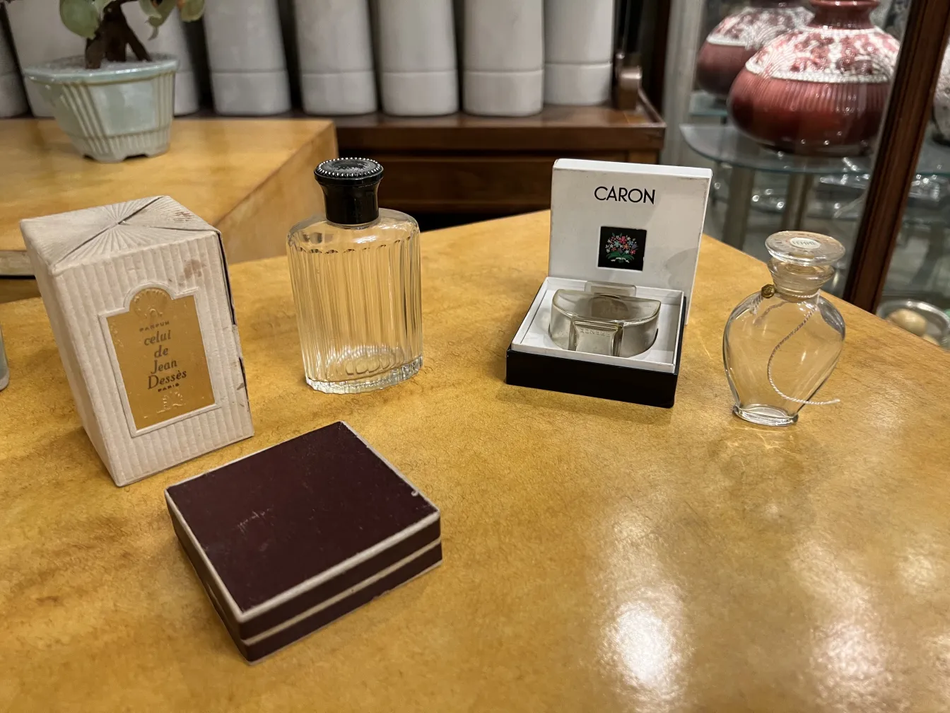 Frasco de perfume antiguo con tapon negro y forma redondeada, sobre fondo amarillo, con otros objetos decorativos.