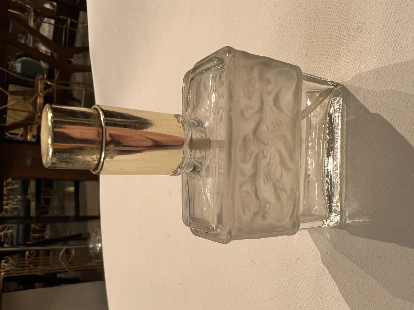 flacone di profumo antico in vetro con tappo lucido, decorato, su un tavolo bianco.