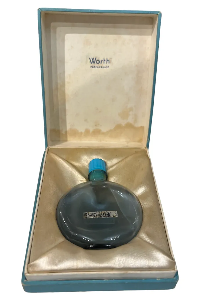 Frasco de perfume antigo redondo com tampa azul em uma caixa elegante.