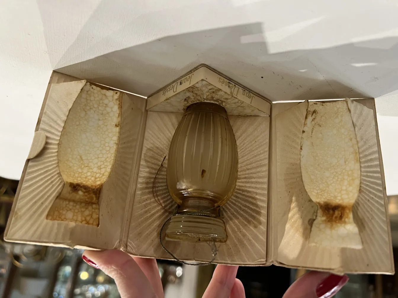 Frasco de perfume antigo em caixa com detalhes. Cor clara e design clássico.