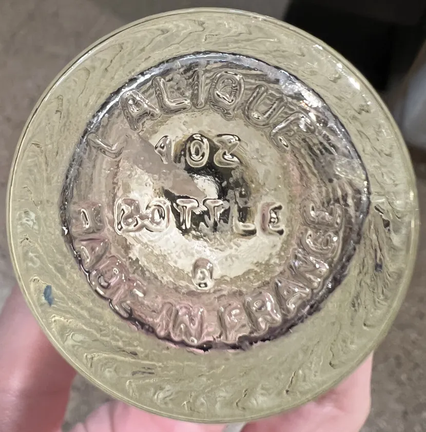 Antique perfume bottle with inscription on the bottom, showing clear details and surroundings.