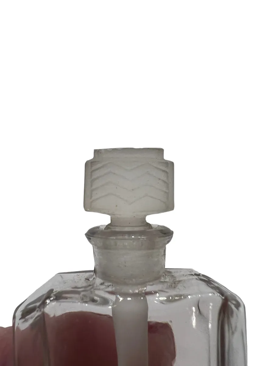 Frasco de perfume antiguo con tapa decorativa, en un fondo claro.