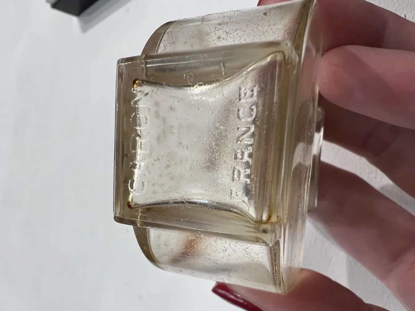 Frasco de perfume antigo segurado na mão, com detalhes visíveis.