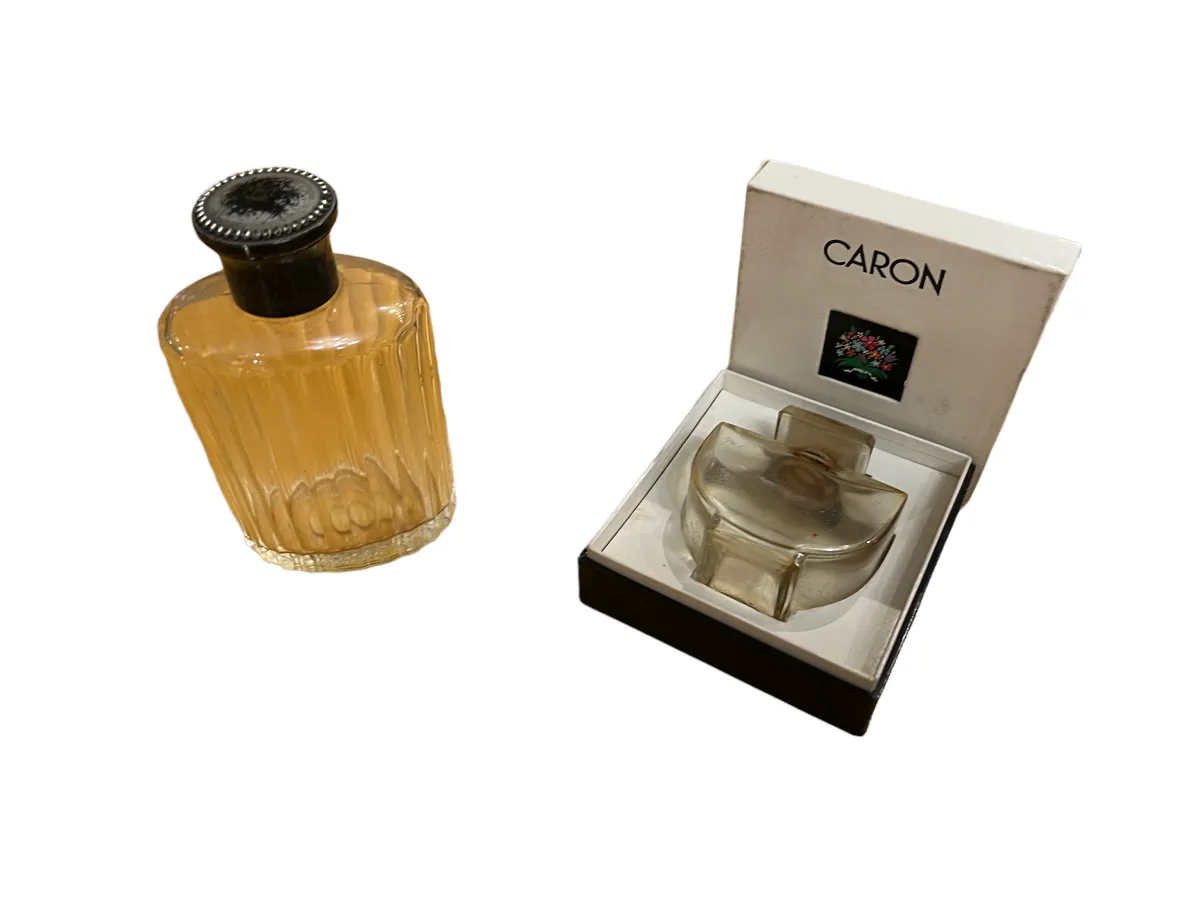 frasco de perfume antigo decorado com linhas verticais e tampa preta, apresentado ao lado de sua caixa