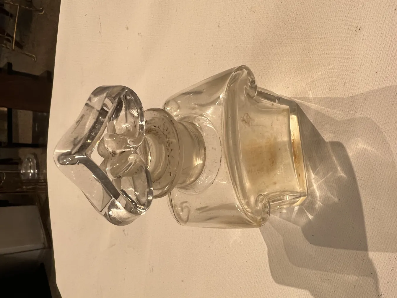 Antique glass perfume bottle with a decorated lid and soft light reflections.