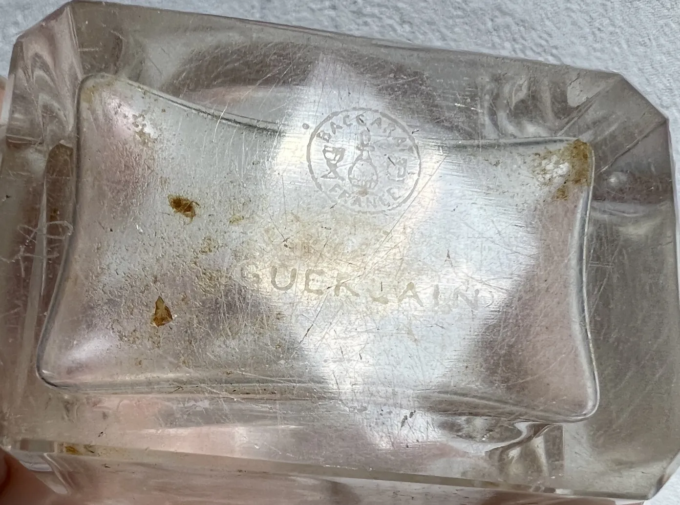 Frasco de perfume antigo em forma retangular, transparente, com sinais de desgaste.