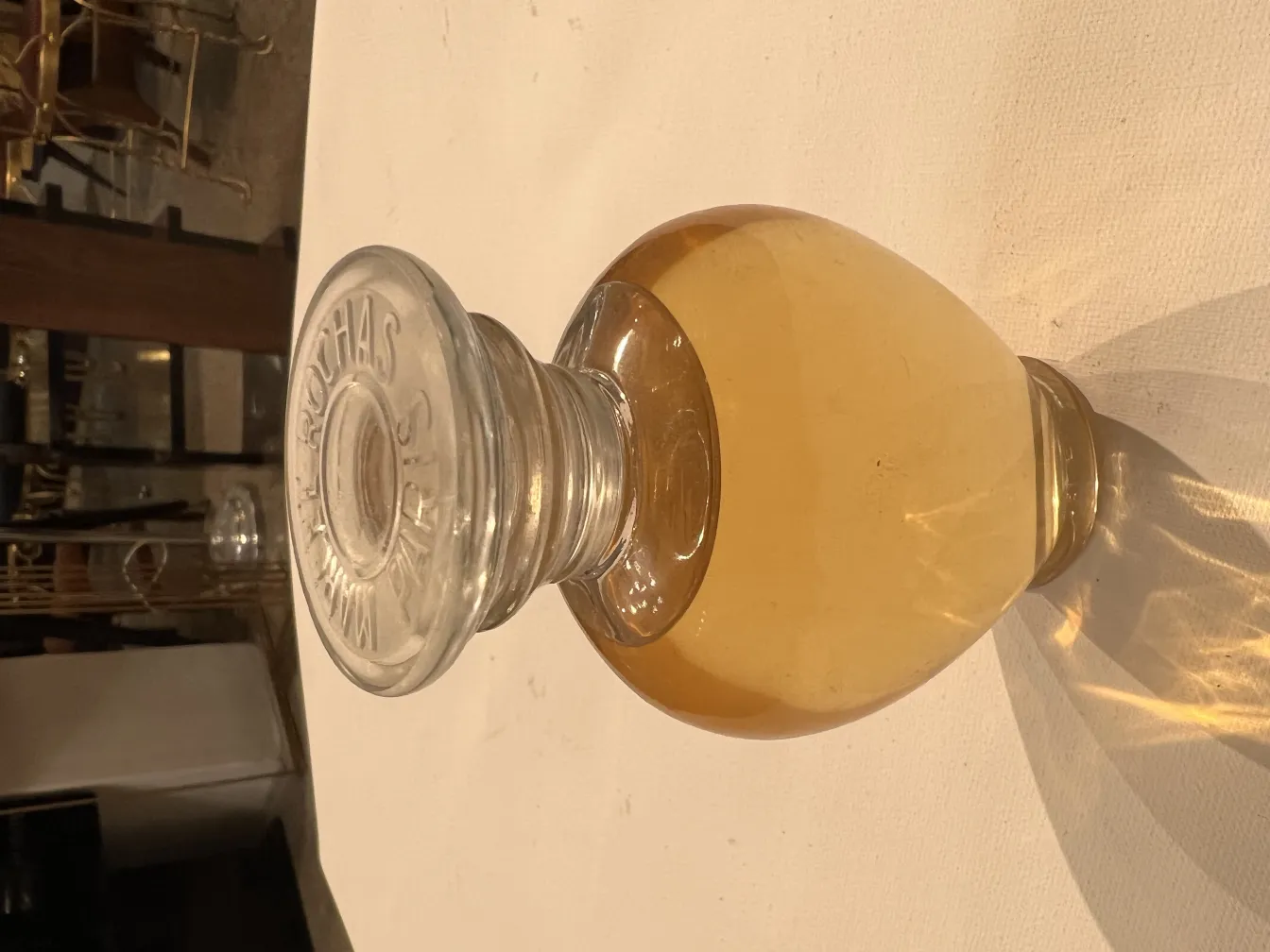 frasco de perfume antigo com líquido dourado e tampa clara em um fundo claro