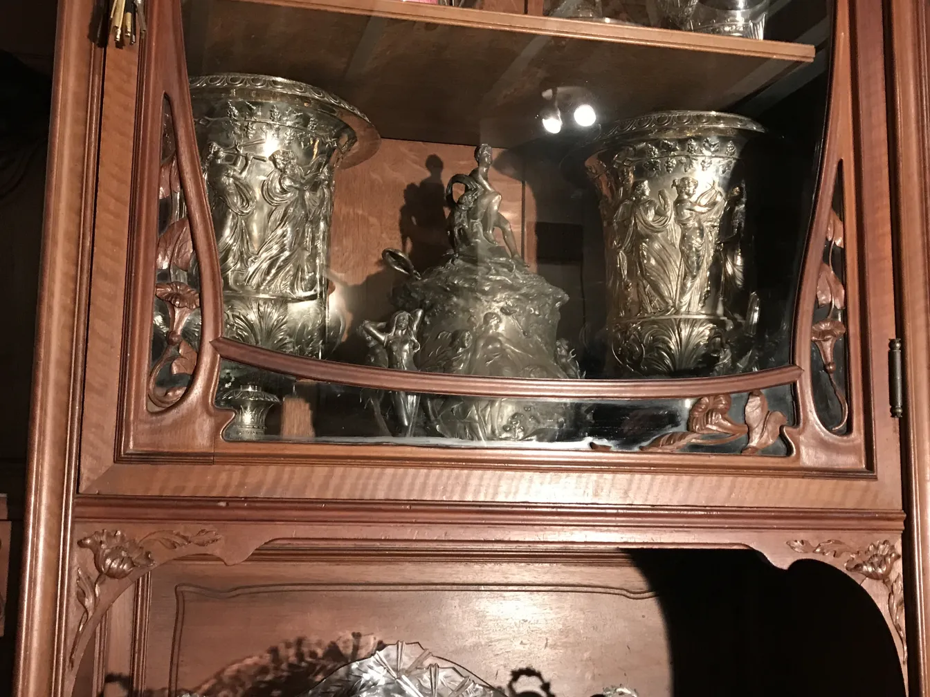 Vitrine ancienne avec des détails décoratifs et des objets argentés à l'intérieur
