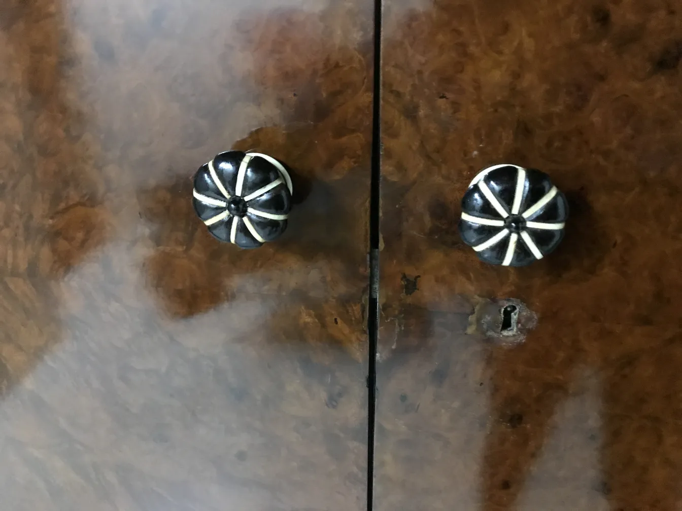 Vetrina antica con due maniglie decorative su uno sfondo in legno chiaro.