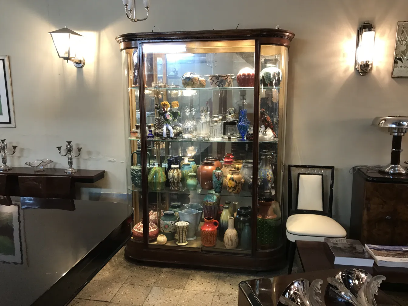 Vitrine antiga com vários itens decorativos e cerâmicas coloridas em um ambiente elegante.