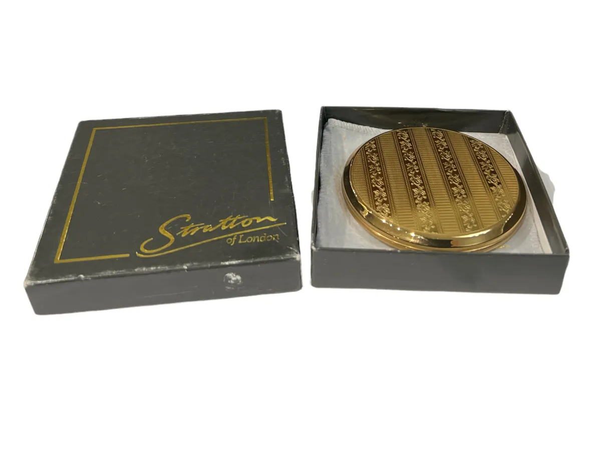 Antique compact with golden finish and decorative details, presented in a black box.