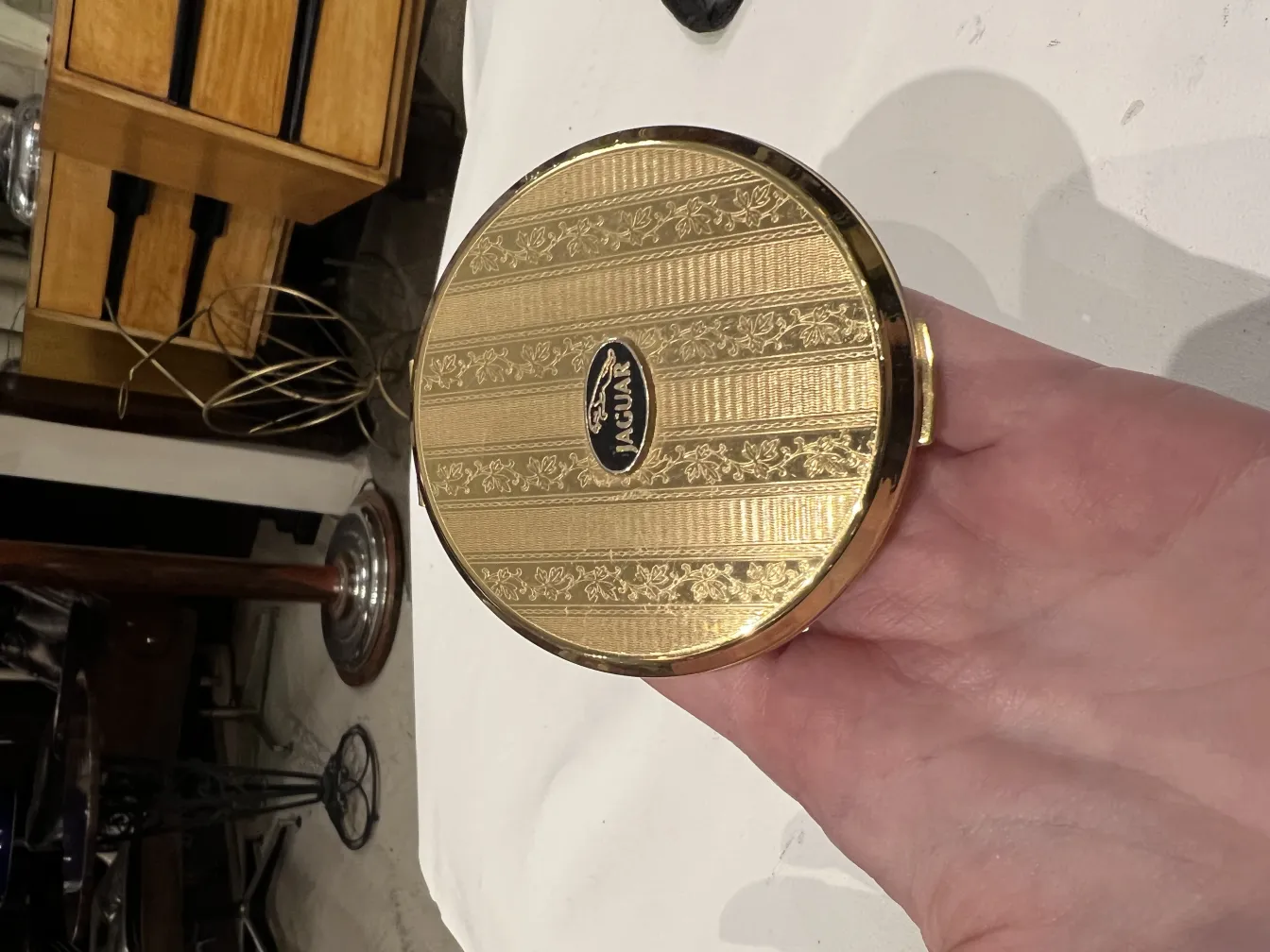 Polvera ancienne avec un design doré et élégant dans une main.