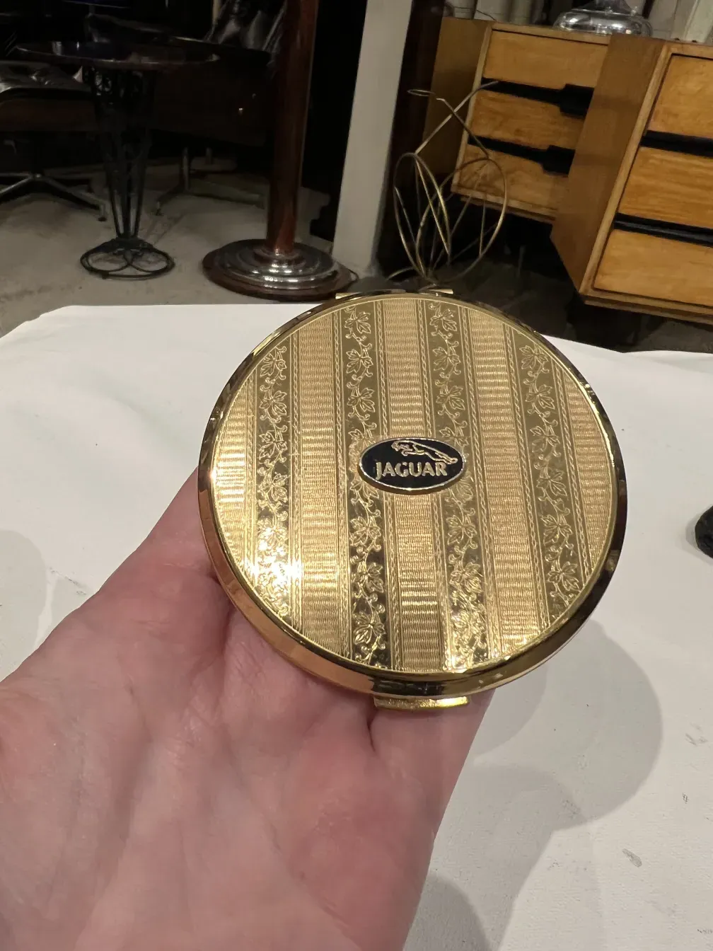 Antike Polvera mit goldenem Design und Jaguar Stratton-Logo auf hellem Hintergrund.
