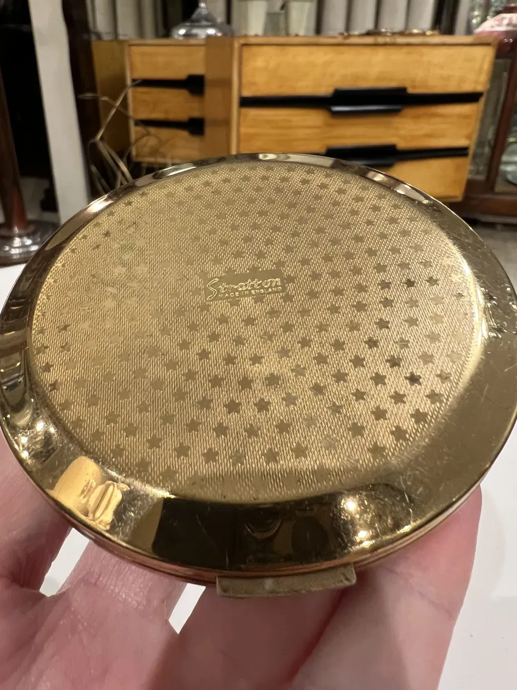 古代のコンパクト Stratton England、金色のデザインが手に持たれています。