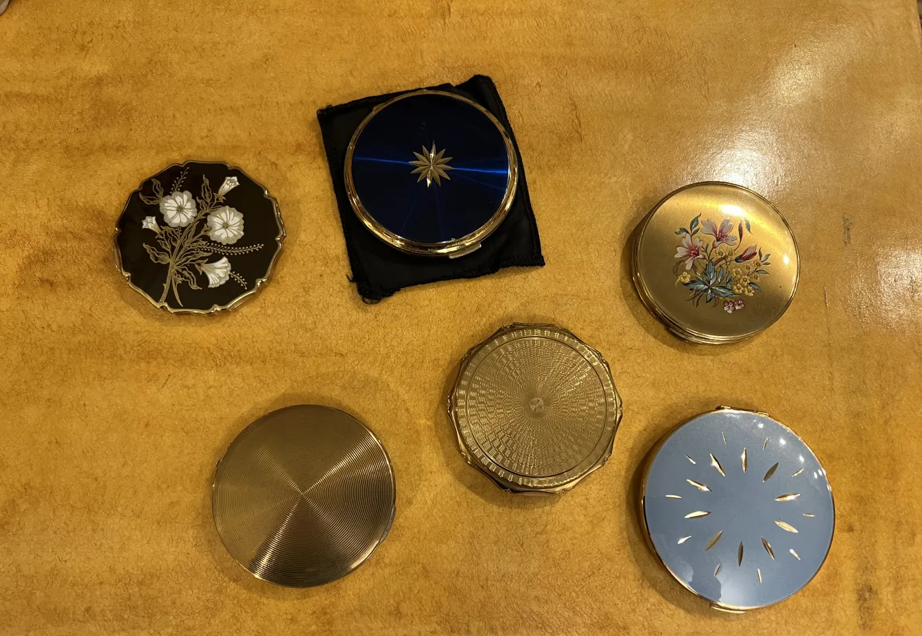 Polvera antiga Stratton England decorada com flores e cores vibrantes, em um ambiente rústico.